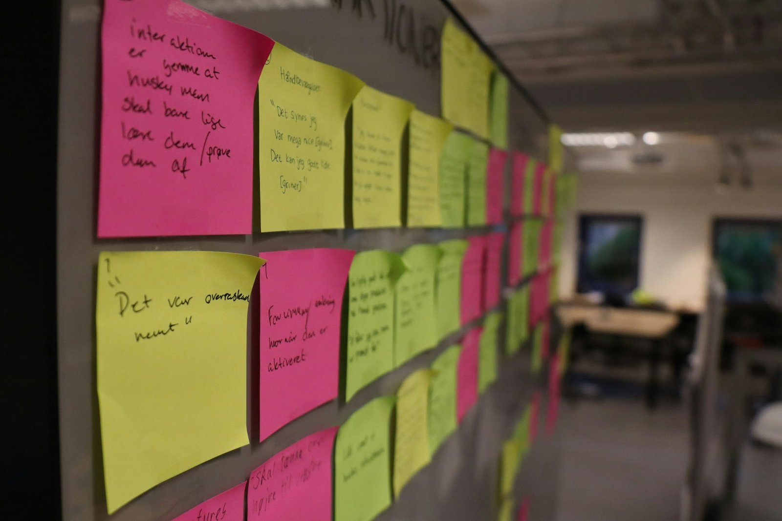 A long corridor wall of pink, yellow and green notes in handwriting, running into the distance