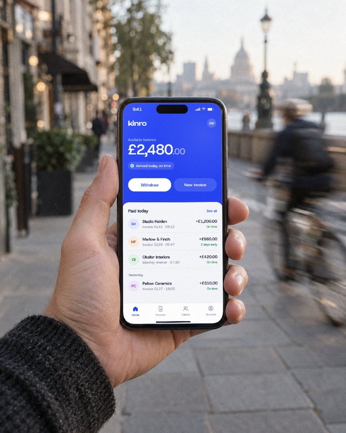 A hand holding a phone showing a Kinro balance of £2,480 on a London street