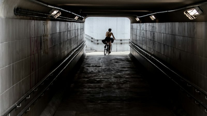 A cyclist riding out of a dark concrete underpass into daylight