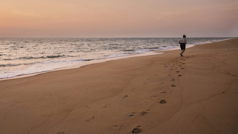 A runner on an empty beach at first light, footprints trailing behind