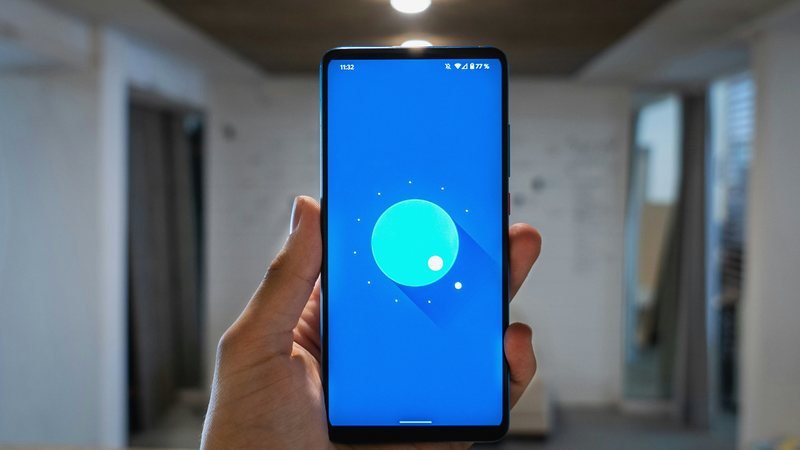 A hand holding a phone with a bright cobalt screen in a softly lit room