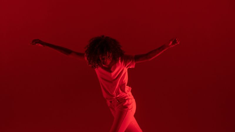 A dancer in red light, arms outstretched mid-turn