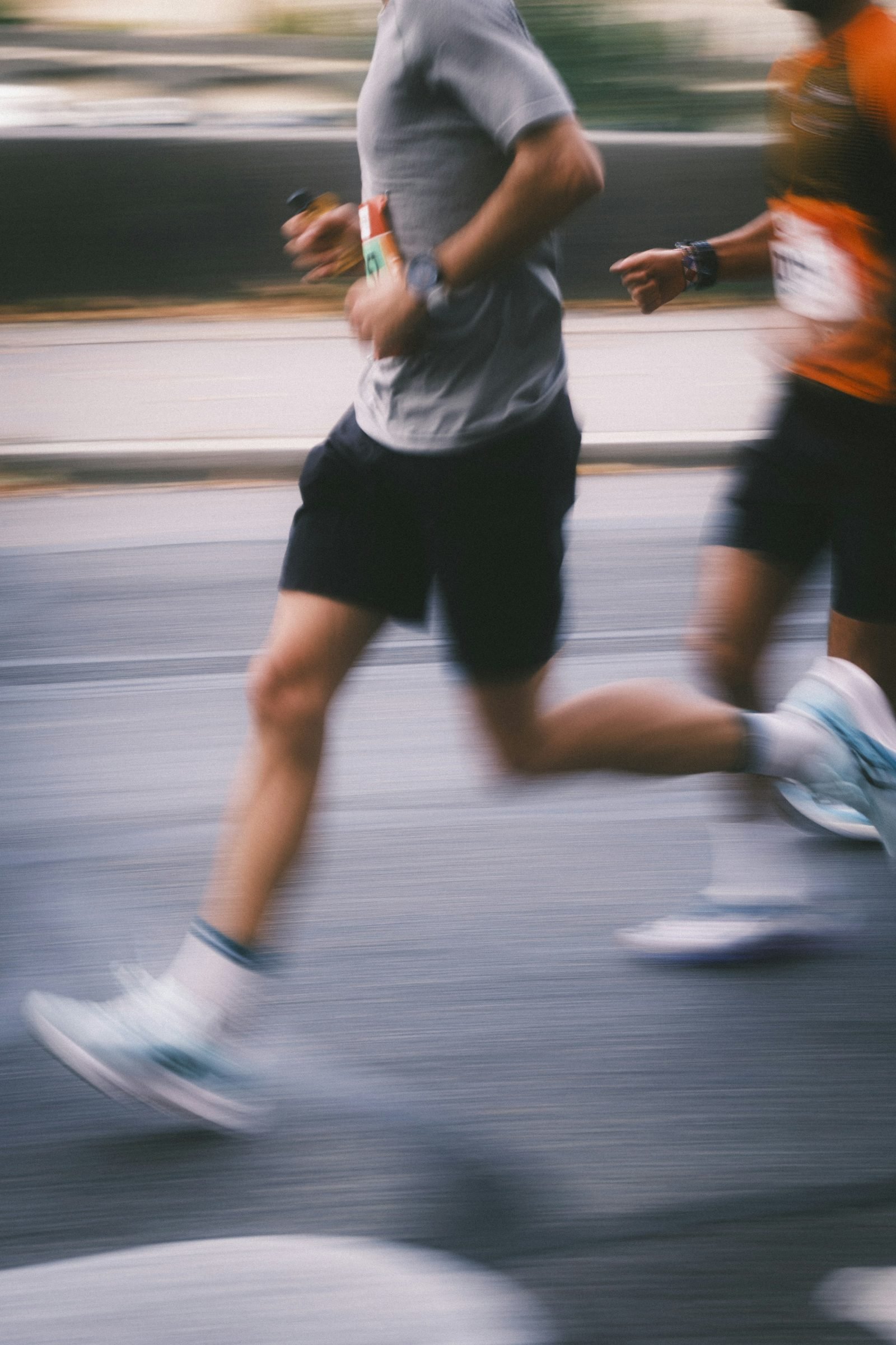 Two runners in grey and orange blurred by speed on a city road